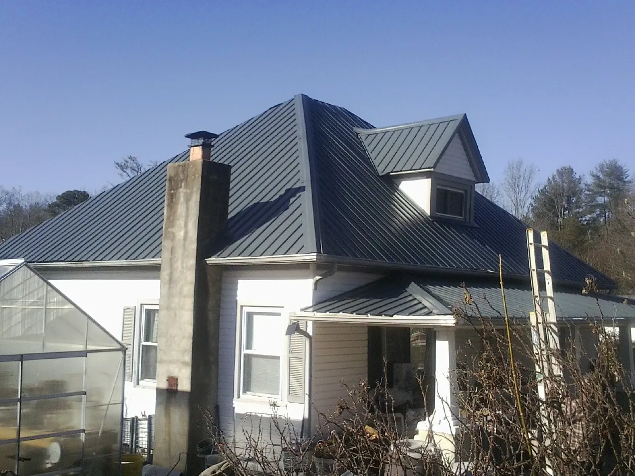 Dark blue standing seam metal roof on a white farmhouse with dormer — Slate & Tile Roof Repair by Roofing Brothers in Olmstead