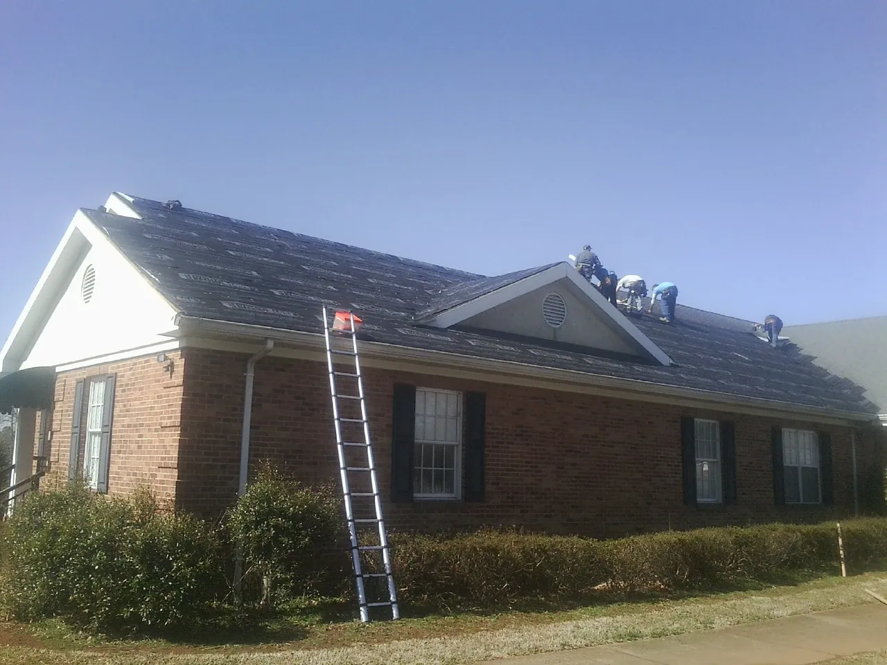 Crew tearing shingles off a brick ranch roof with a ladder set — Emergency Roof Repair work by our crew in Olmstead