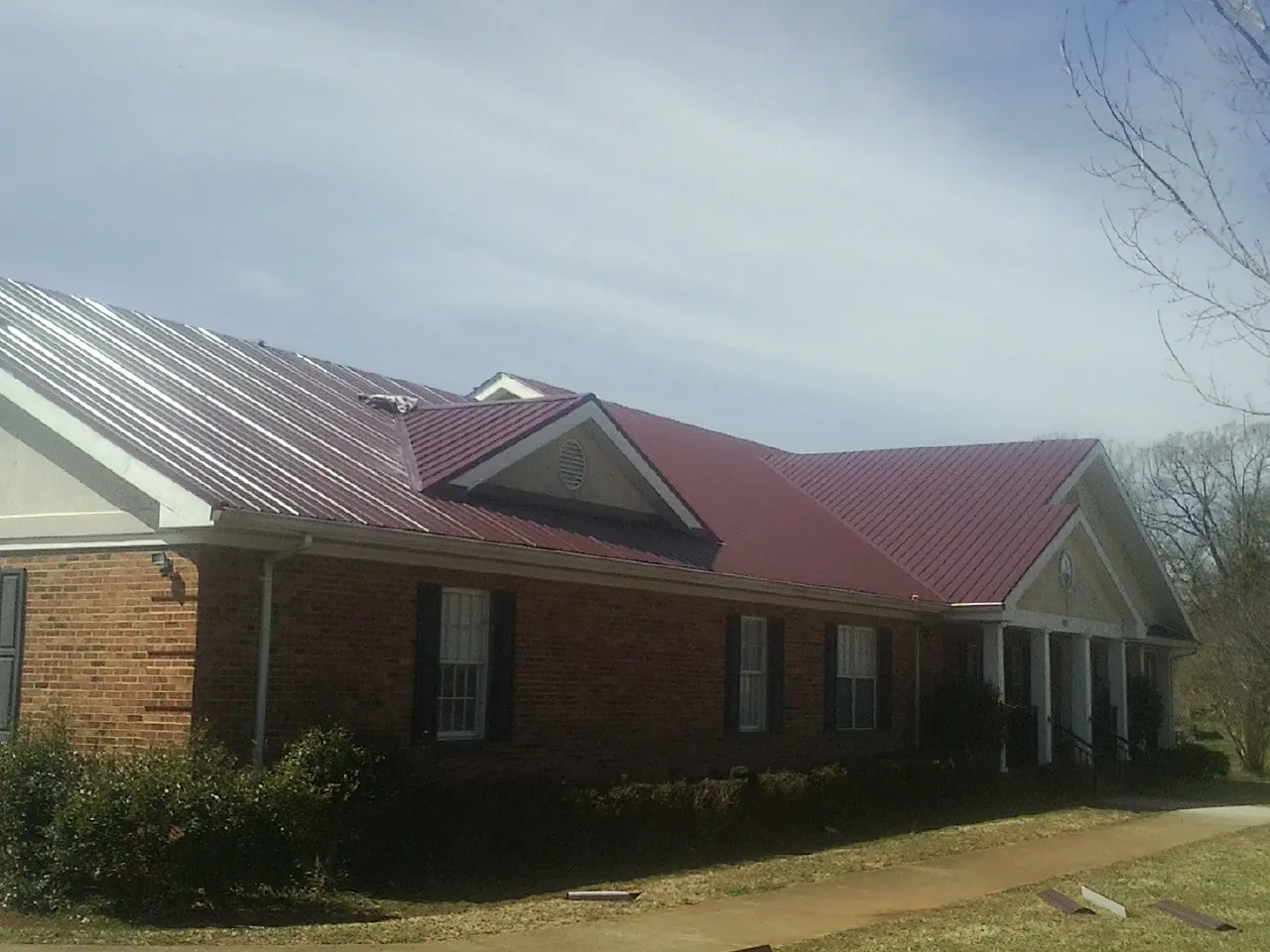 Red metal roof with gabled entries on a long brick building, from a Hail Damage Roof Repair job in Olmstead