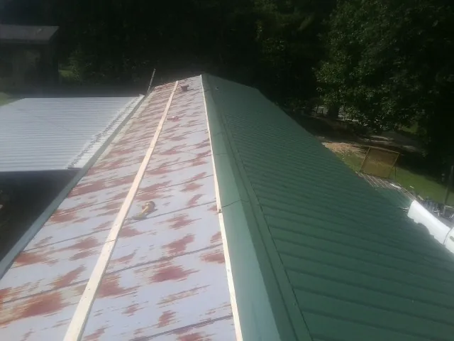 Old rusted panels beside newly installed green metal roofing — Wind Damage Roof Repair by Roofing Brothers in Olmstead