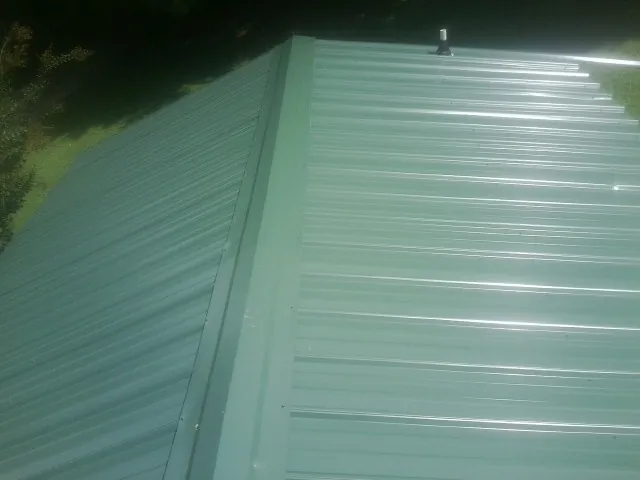 New green metal panels meeting at the ridge of a roof — Flat Roof Repair work by our crew in Olmstead