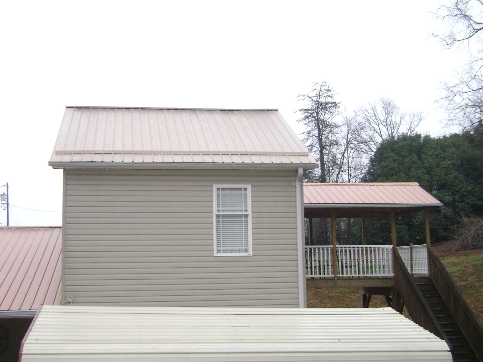 Tan metal roofs on a two story addition and attached porch, from a Roof Replacement job in Olmstead
